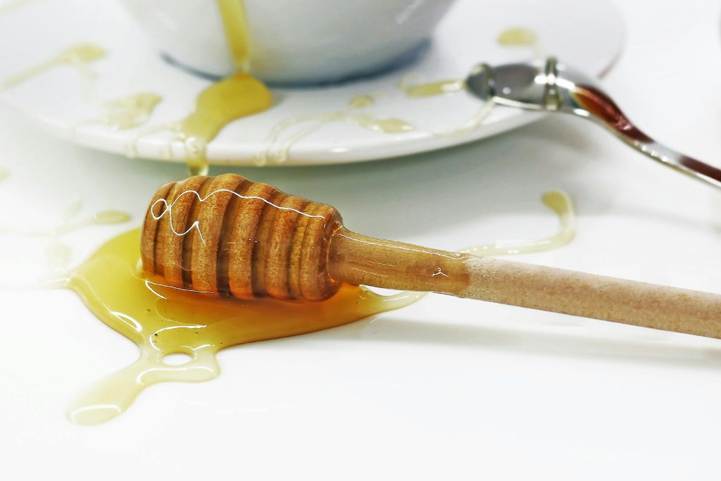 Close-up of a honey dripper with spilled honey on a white surface, creating a sweet mess.